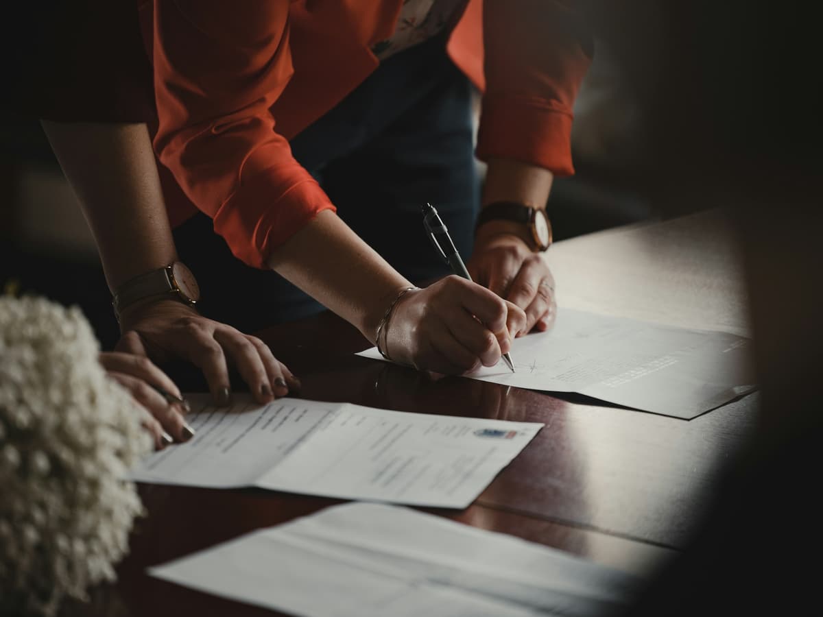 Two people reviewing and signing commercial documents at a wooden table