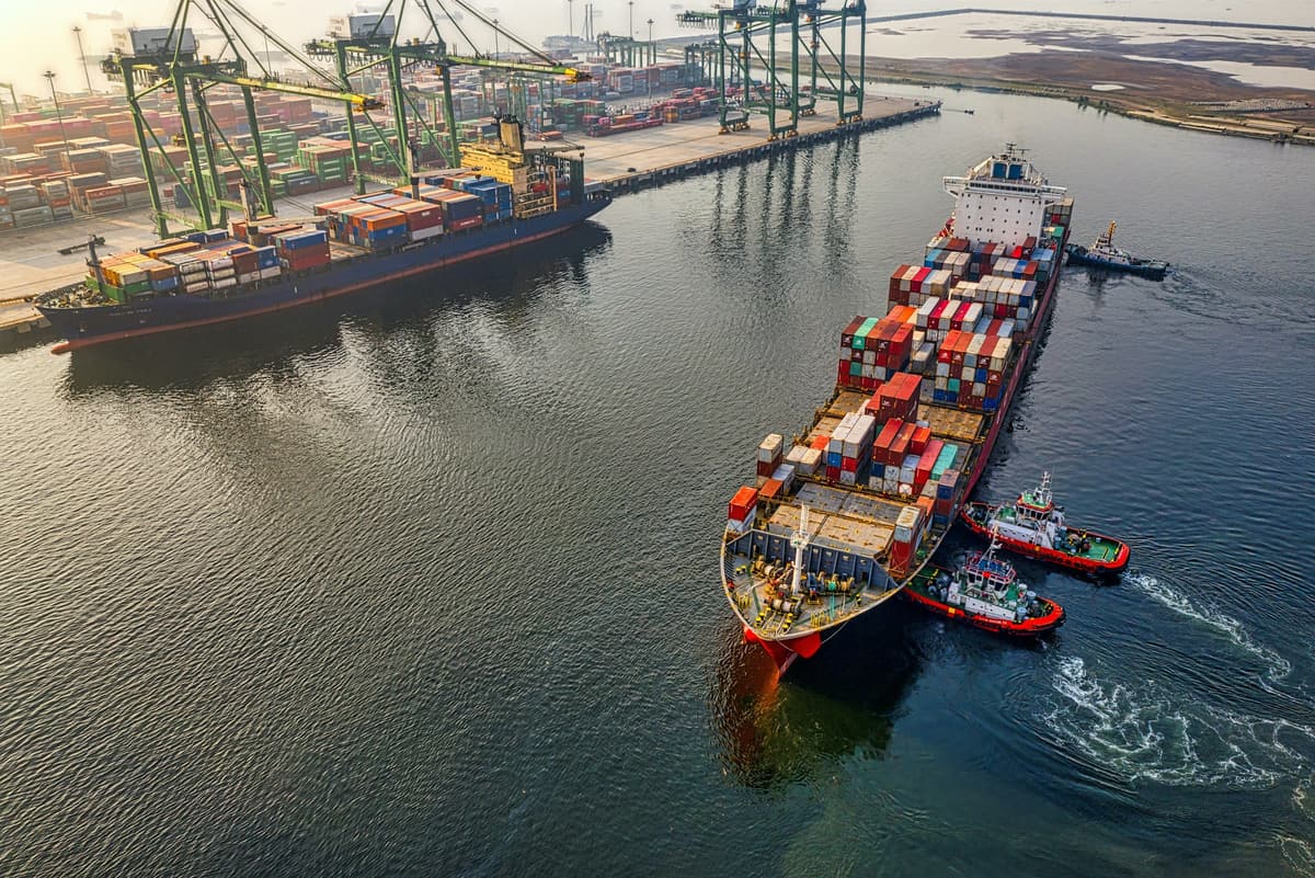 A loaded container ship guided by two tugboats as it leaves a container terminal